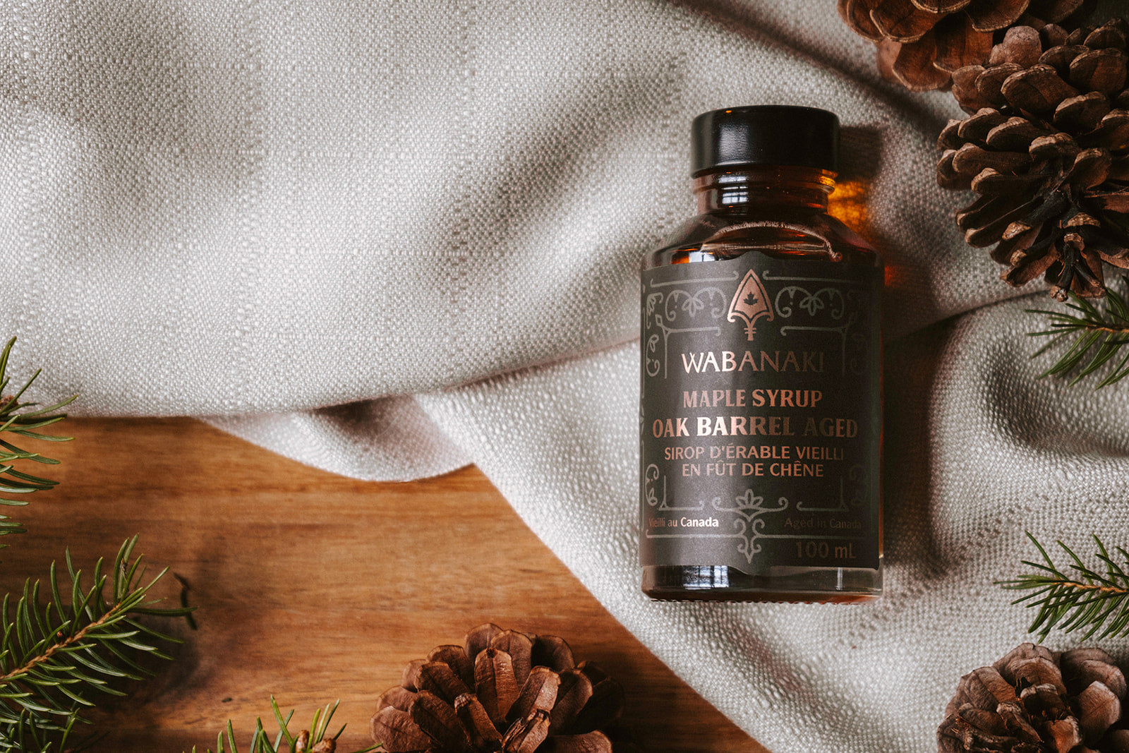 Wabanaki Maple Syrup pictured on a white cloth. This maple syrup is 100% Indigenous, female owned maple syrup company from Canada with barrel aged maple syrup and Golden Grade A available